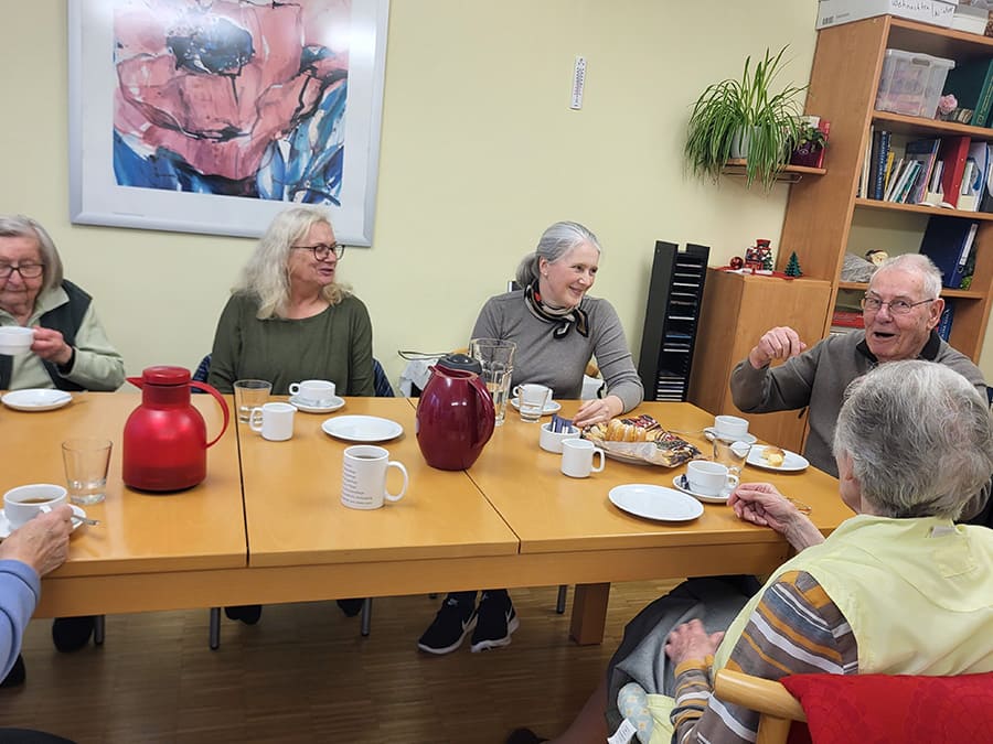 An einem Tisch sitzt eine Gruppe von älteren Menschen die zusammen Kuchen essen, Kafee trinken und sich unterhalten